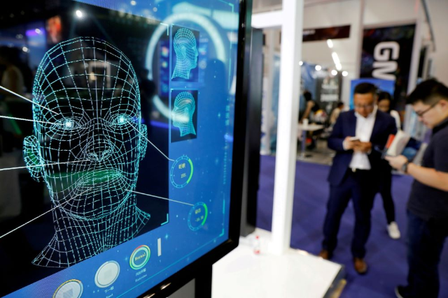 Visitors check their phones behind the screens advertising facial recognition software during Global Mobile Internet Conference at the National Convention in Beijing, China April 27, 2018